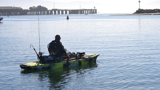 Person fishing from a kayak on calm water with a pier in the background
